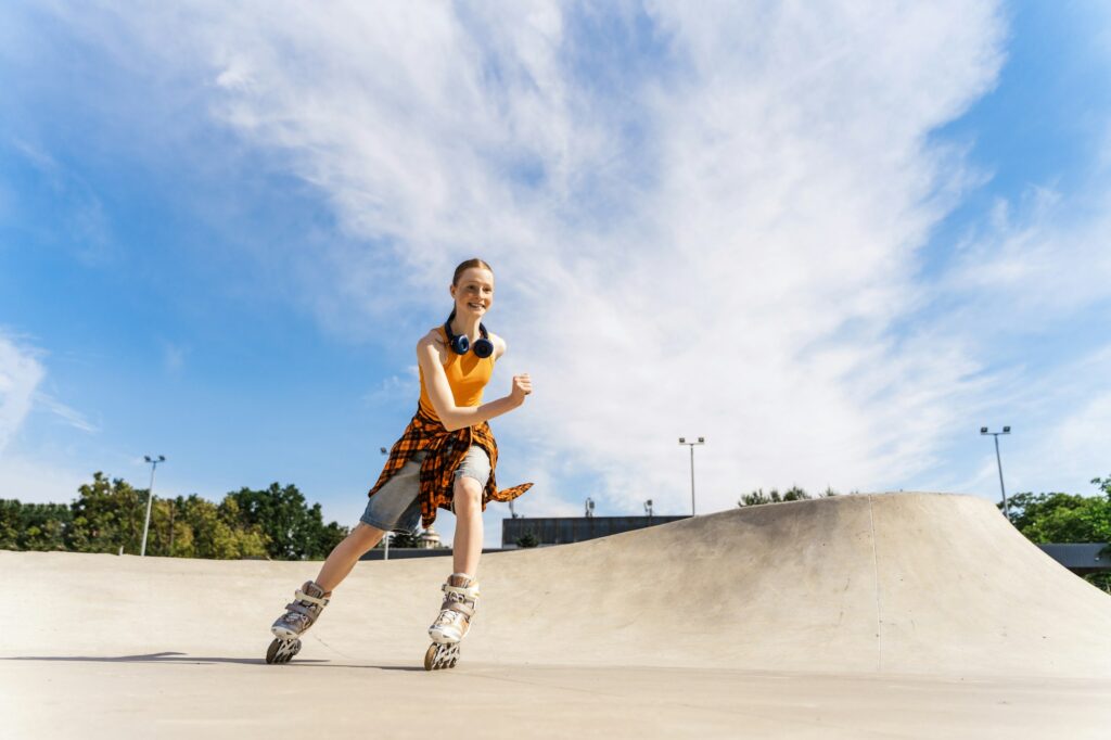 Pretty teenage girl rollerskating in public park using headphones